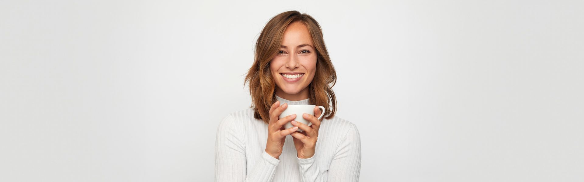 Eine Frau hält eine Tasse Kaffee in ihren Händen und lächelt | Zahnmedizin am Neckar