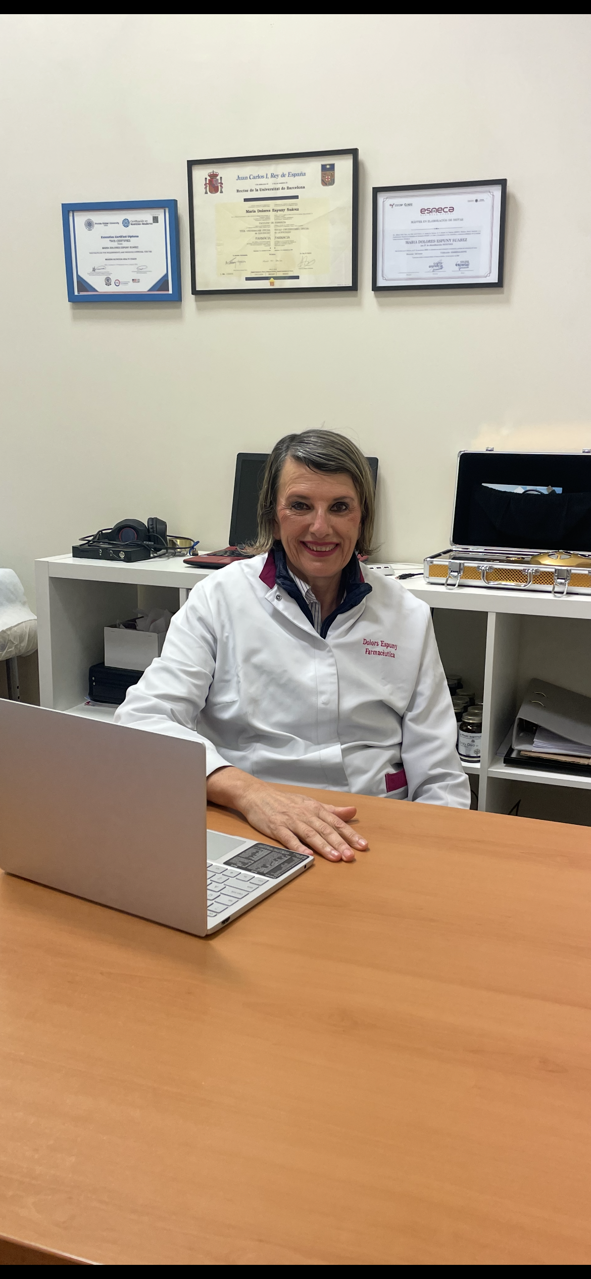 Una mujer con una bata de laboratorio está sentada en un escritorio con una computadora portátil.