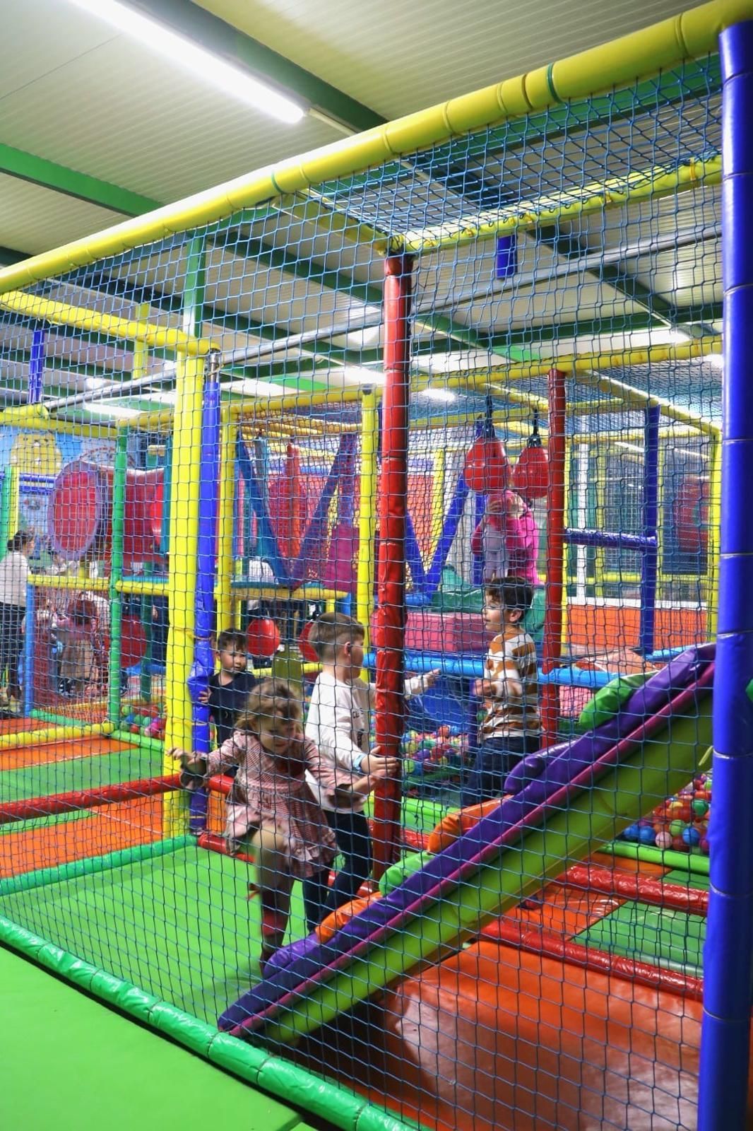 Parque infantil interior con piscina de pelotas de colores, estructuras para escalar y túneles.