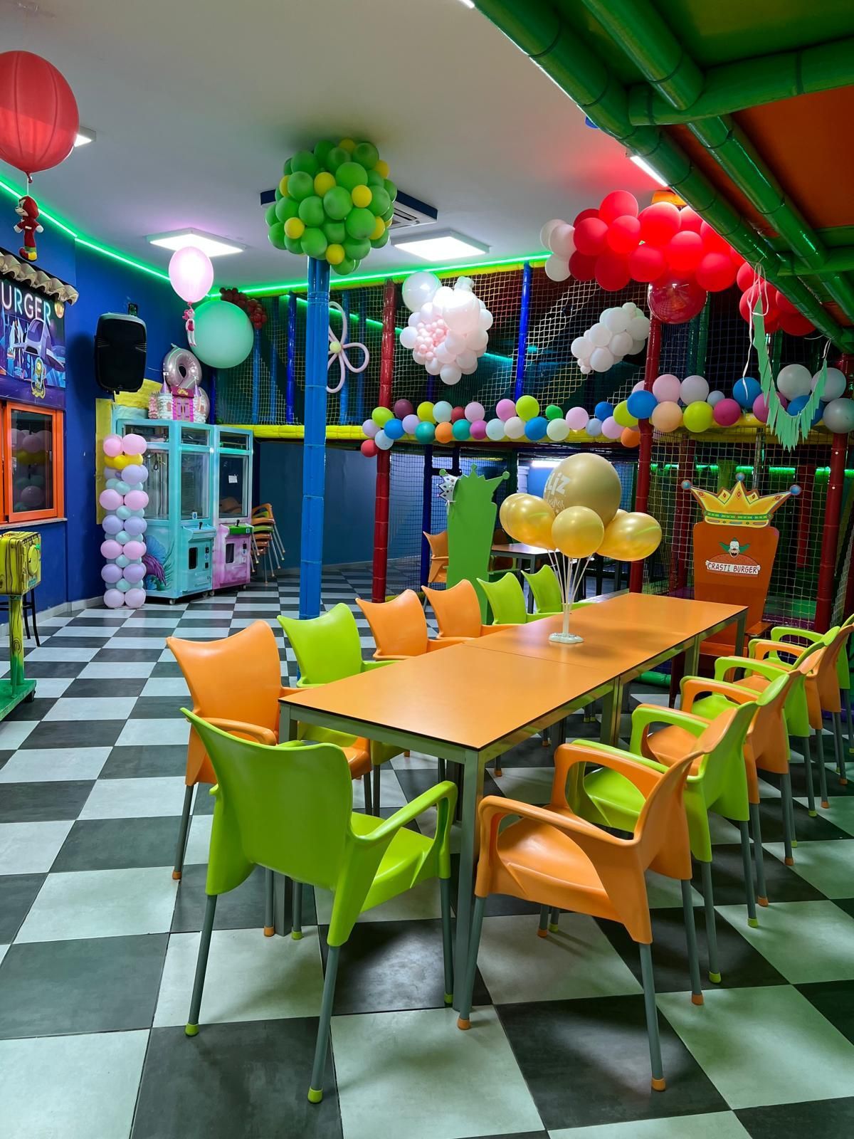 Comedor con suelo a cuadros, sillas naranjas y verdes, techo a cuadros y filas de mesas.