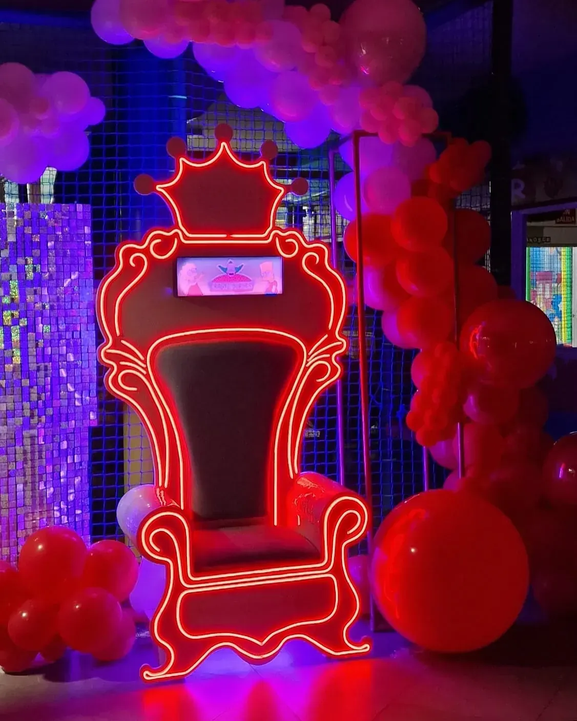 Trono rojo neón rodeado de globos, decoración de fiesta.