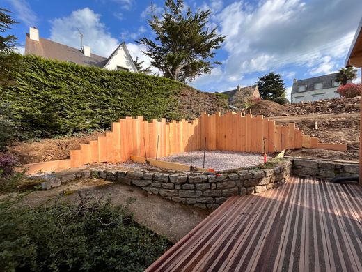 Chantier de construction dans un jardin, avec un mur de soutènement en bois et une terrasse sous un ciel bleu