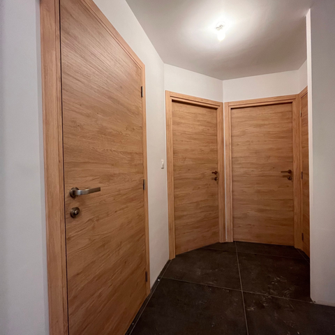 Couloir lambrissé avec trois portes en bois fermées et un sol carrelé foncé.