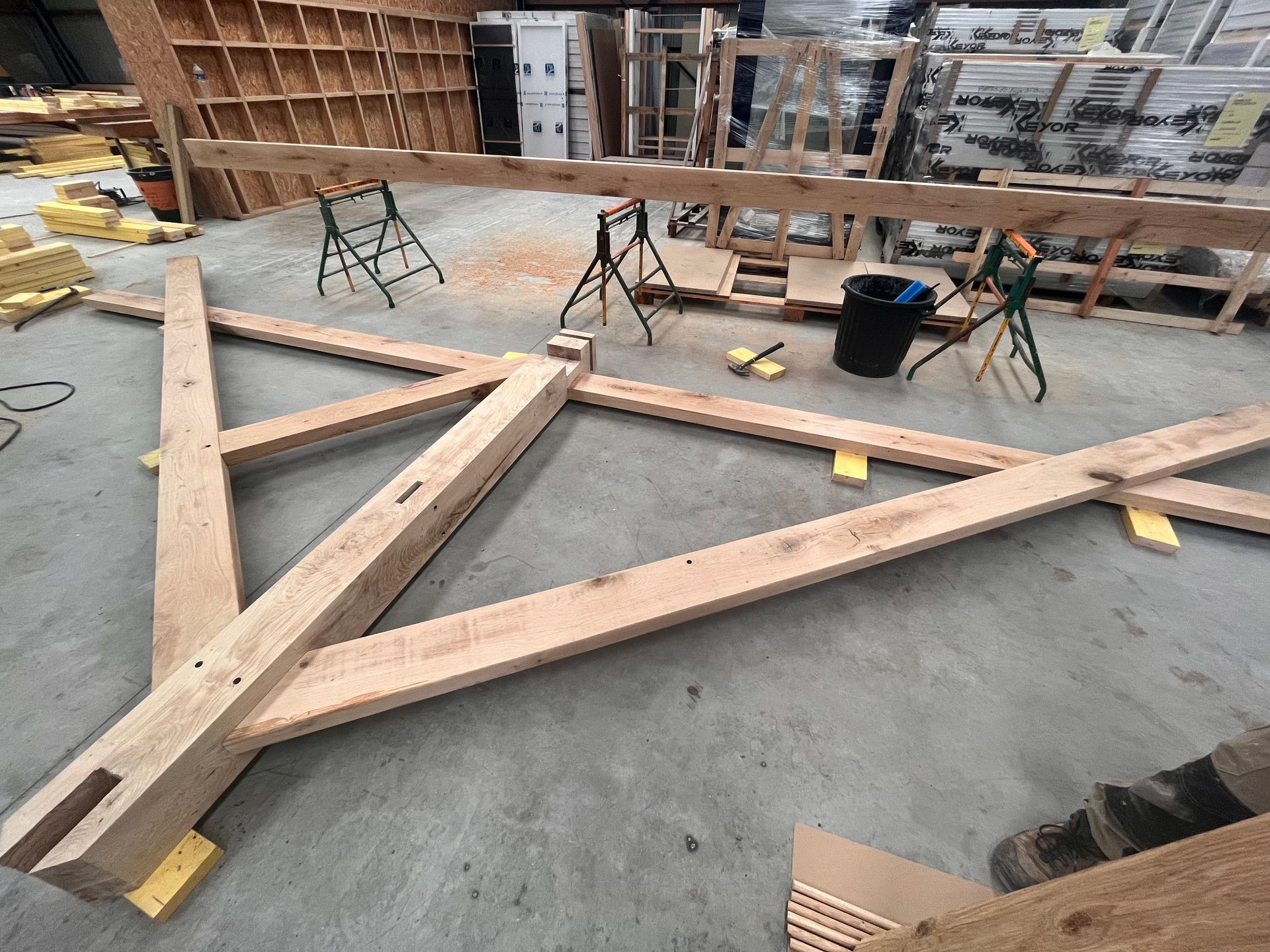 Cadre triangulaire en bois en cours de fabrication dans un atelier, avec des serre-joints, des outils et un seau à proximité.