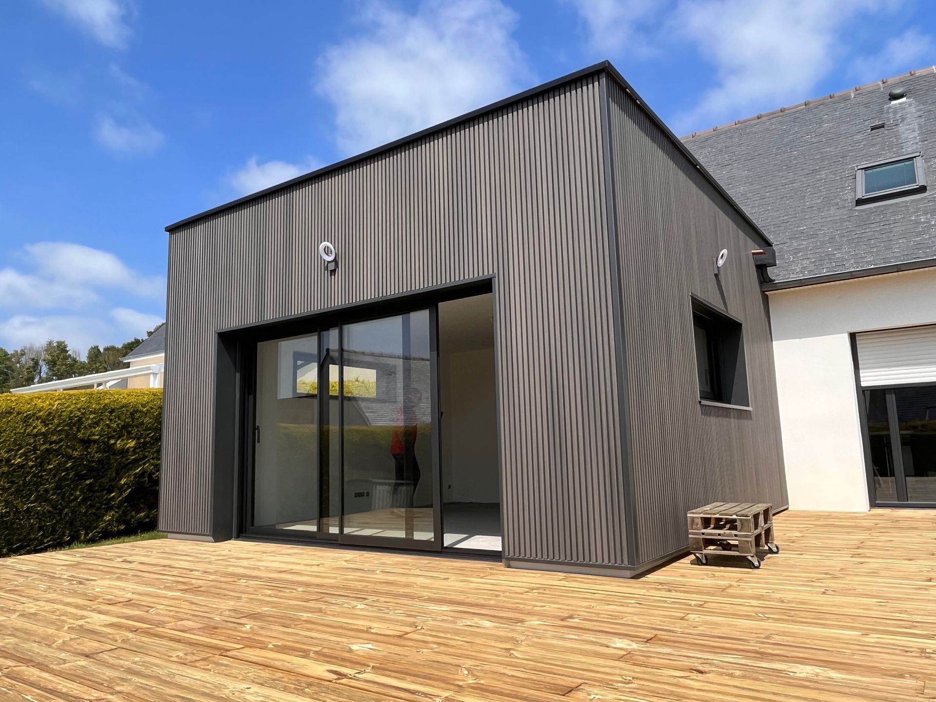 Pièce de patio moderne dans un jardin, avec un bardage en bois foncé et de grandes baies vitrées coulissantes.