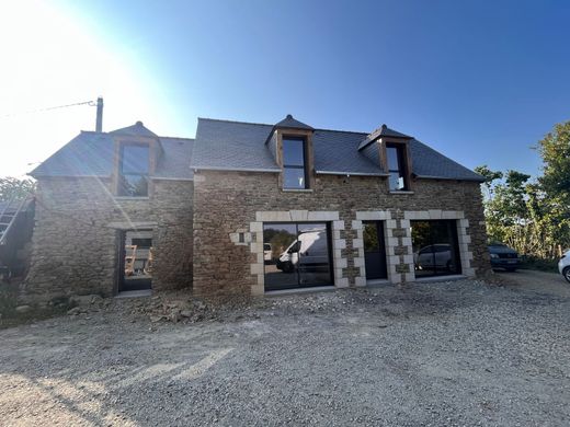 Maison en pierre avec un toit en ardoise et de grandes fenêtres sous un ciel bleu dégagé, avec une allée en gravier devant