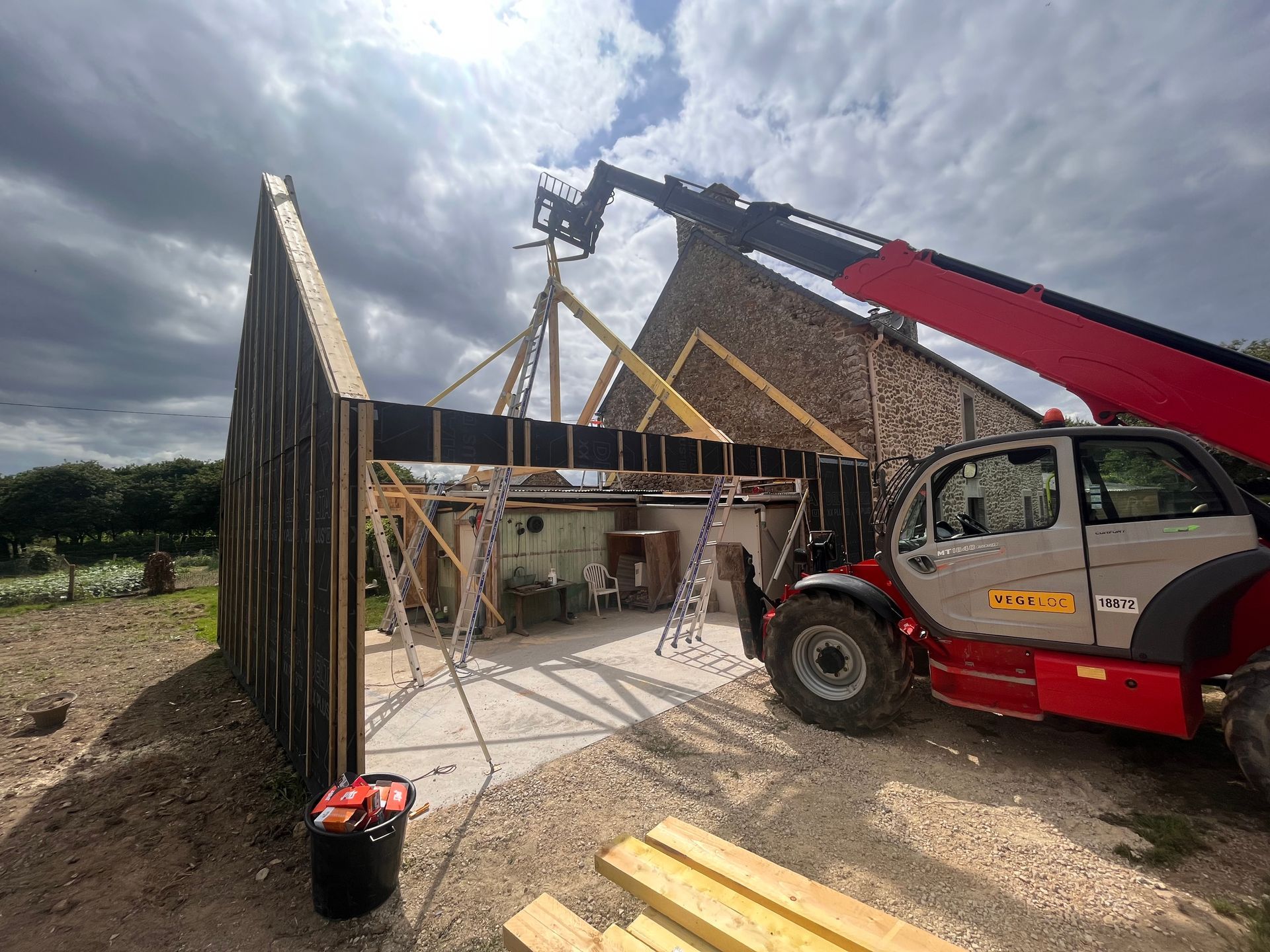 Grue rouge soulevant une ferme de toit sur l’ossature d’une maison, sur un chantier sous un ciel nuageux