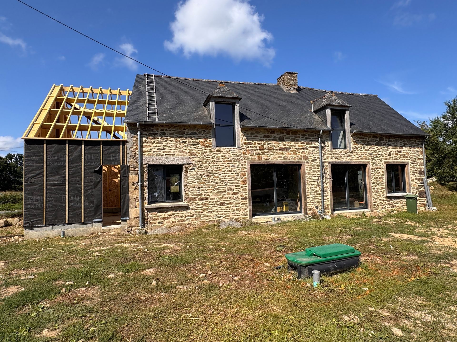Ferme en pierre en cours de rénovation, avec la charpente apparente et un ciel bleu au-dessus