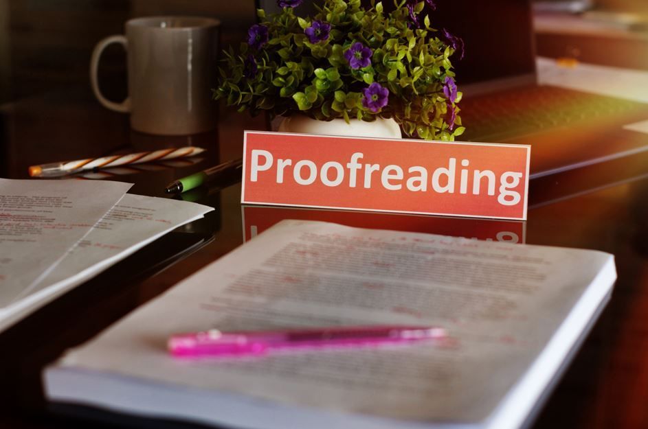 Cartel de corrección de pruebas sobre un escritorio con un libro, un bolígrafo y una planta.