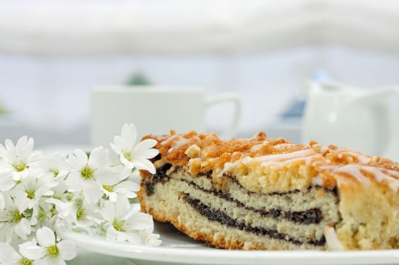 Ein Stück Kuchen liegt auf einem weißen Teller neben weißen Blumen