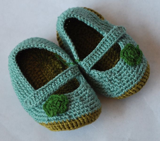 Ein Paar gehäkelte Babyschuhe mit grünen Blättern darauf