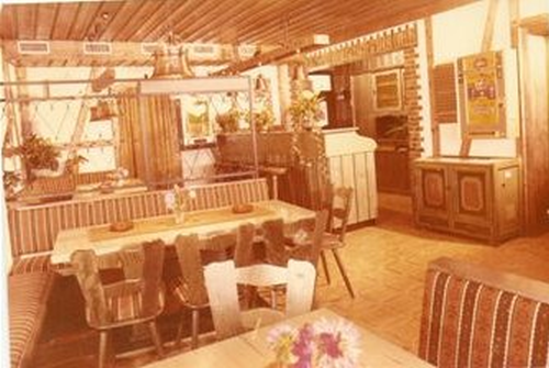 Interieur eines Restaurants mit Holztischen, Stühlen und dekorativen Holzbalken. Warme Farbtöne und rustikales Ambiente.