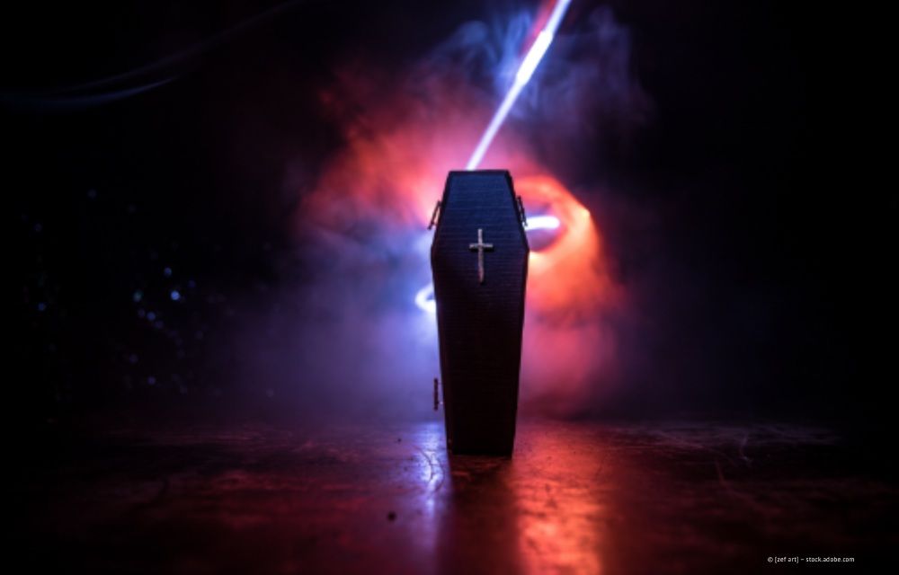 Sarg mit Kreuz, rot und blau beleuchtet, umgeben von Rauch.
