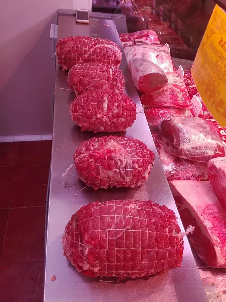 Trozos de carne roja envueltos en una red blanca, expuestos en el mostrador de una carnicería.