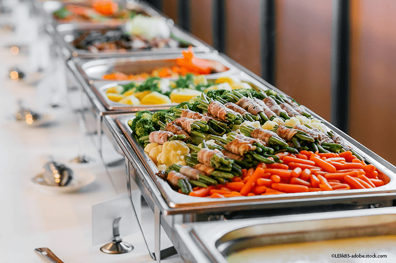 Buffet mit verschiedenen Gemüsegerichten auf Serviertabletts aus Edelstahl.