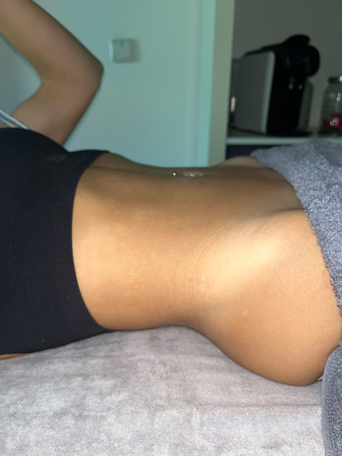 Persona tumbada en una cama con una manta gris, de perfil, con el torso y un brazo levantado a la vista.