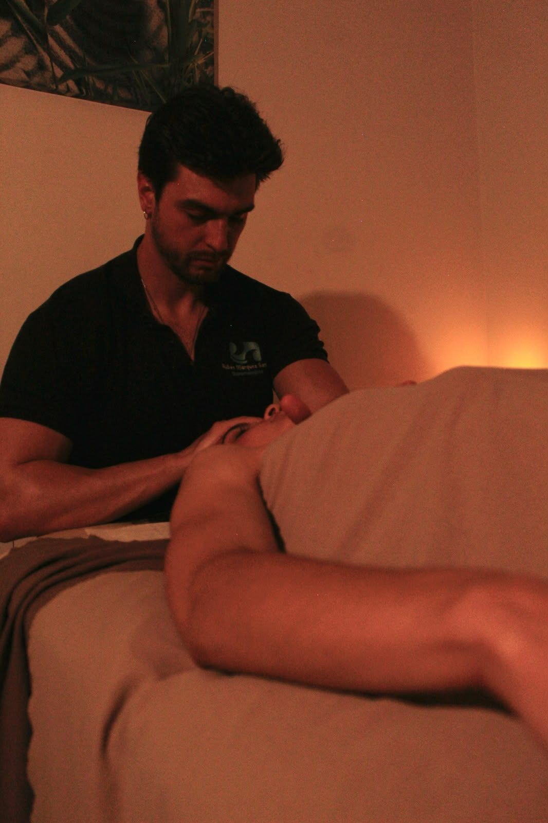Masajista trabajando con un cliente en una sala de tratamiento cálida y con poca luz