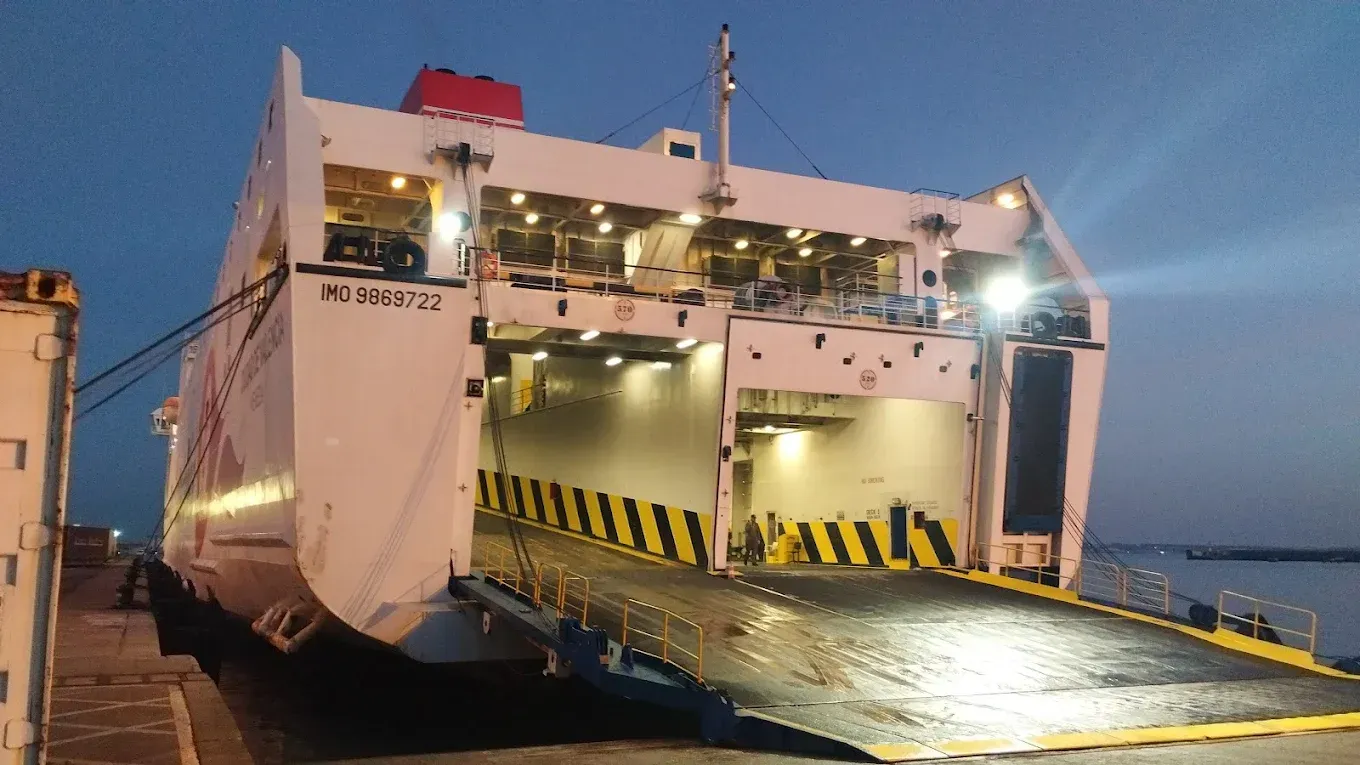 Un ferry blanco atracó al anochecer, con su gran rampa bajada hasta el suelo para la carga.