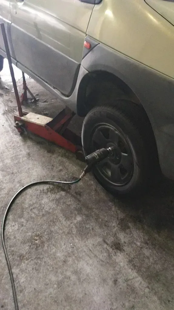 Un coche está elevado sobre un gato rojo mientras se utiliza una llave de impacto neumática.