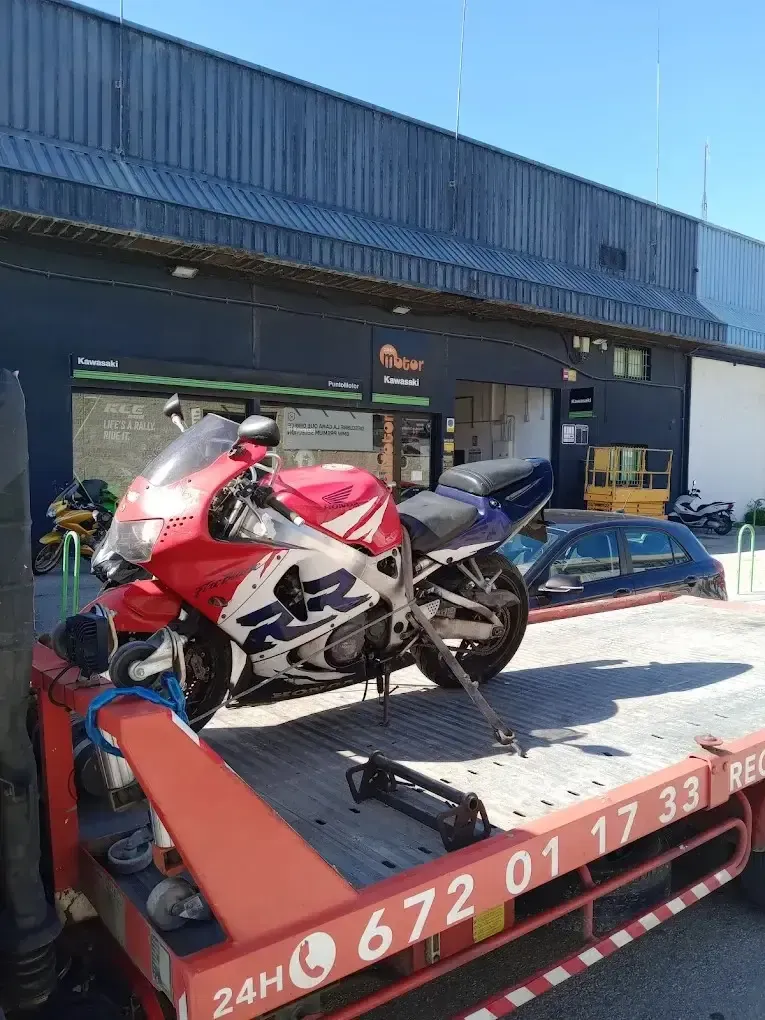 Una motocicleta deportiva Honda CBR roja, blanca y azul, asegurada sobre una grúa de plataforma frente a un almacén.