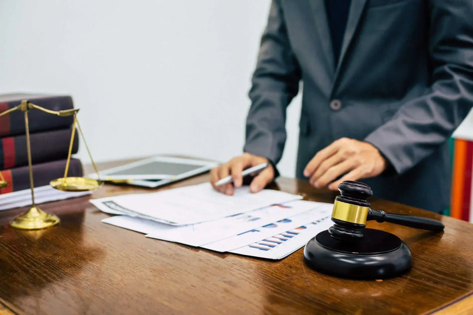 Una persona con traje revisa documentos en un escritorio con un mazo, una balanza de la justicia y una tablilla.