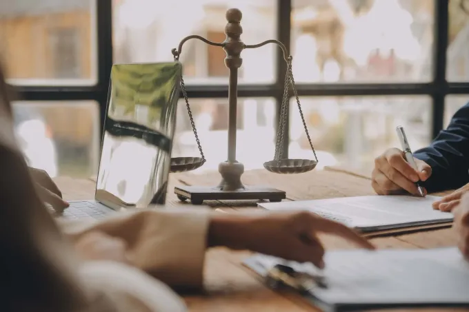 Balanza de la justicia sobre un escritorio con documentos y gente firmando.