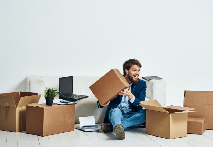 Un hombre está sentado en el suelo rodeado de cajas de cartón.
