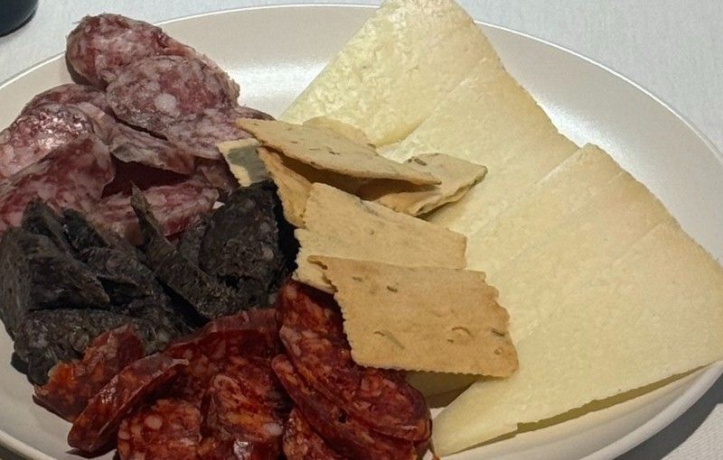 Plato de charcutería con carnes en rodajas, queso y galletas.