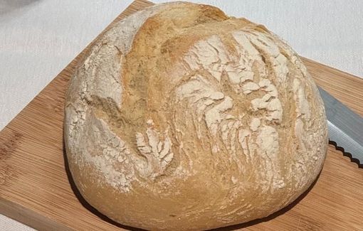 Hogaza redonda de pan sobre una tabla de cortar de madera con un cuchillo de sierra.