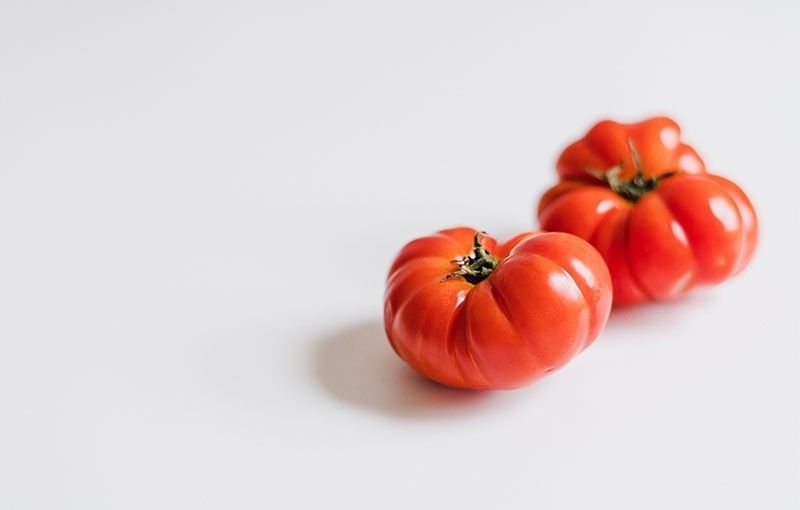 Dos tomates reliquia maduros y rojos sobre una superficie blanca.