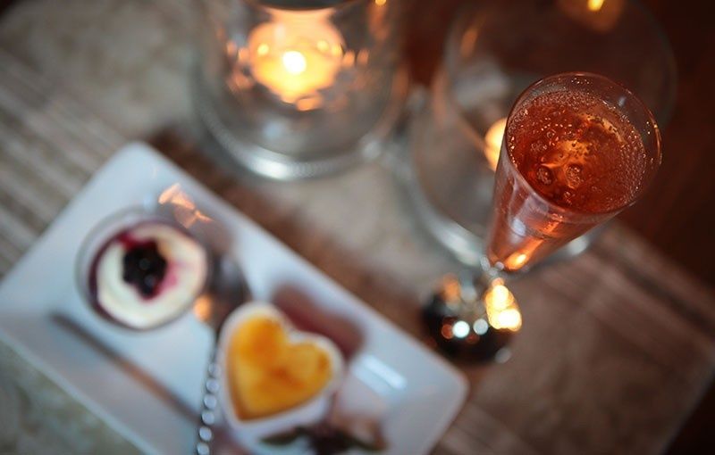 Cóctel y postres en una mesa, iluminada por velas; incluye una copa de champán, natillas y una baya.