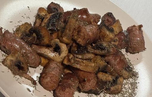 Plato de salchichas y champiñones con hierbas en un plato blanco.