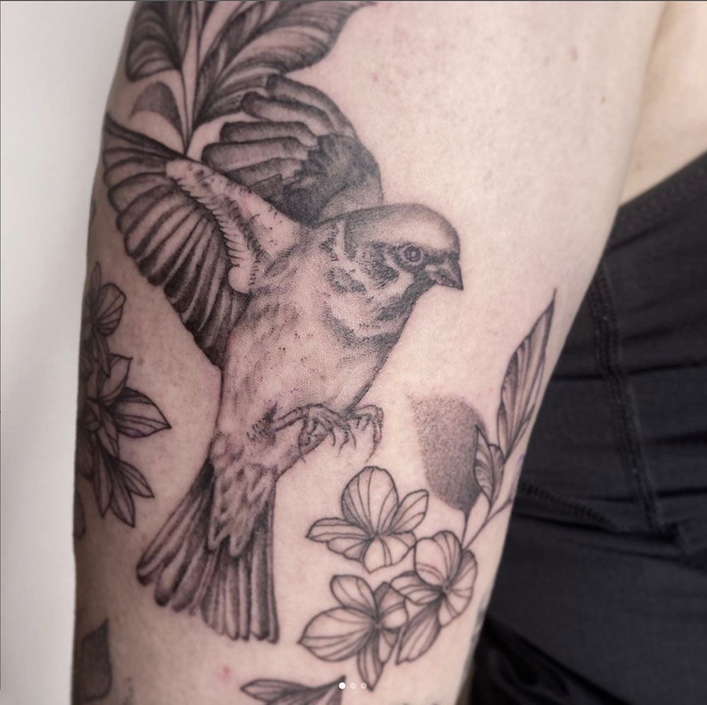 Ein schwarz-weißes Tattoo eines Vogels, umgeben von Blumen