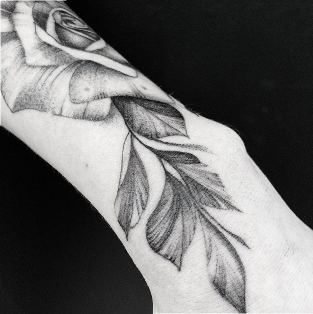 Eine Frau hat eine Tätowierung mit einer Rose und Blättern auf ihrem Arm