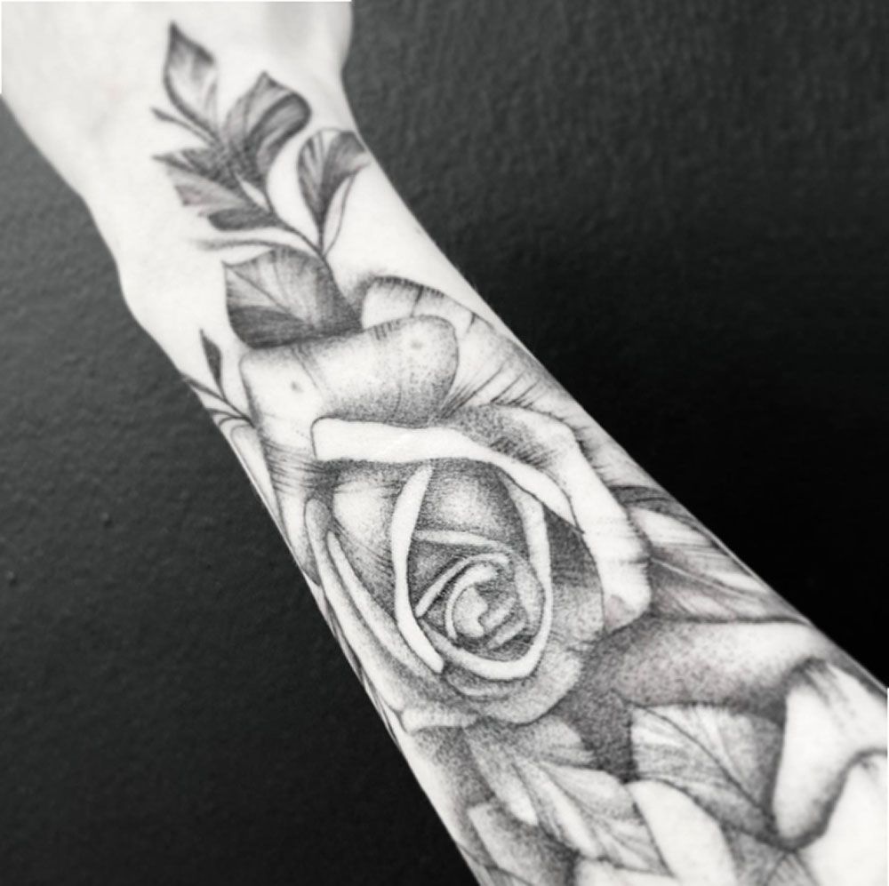 Ein schwarz-weißes Tattoo einer Rose auf dem Arm einer Person