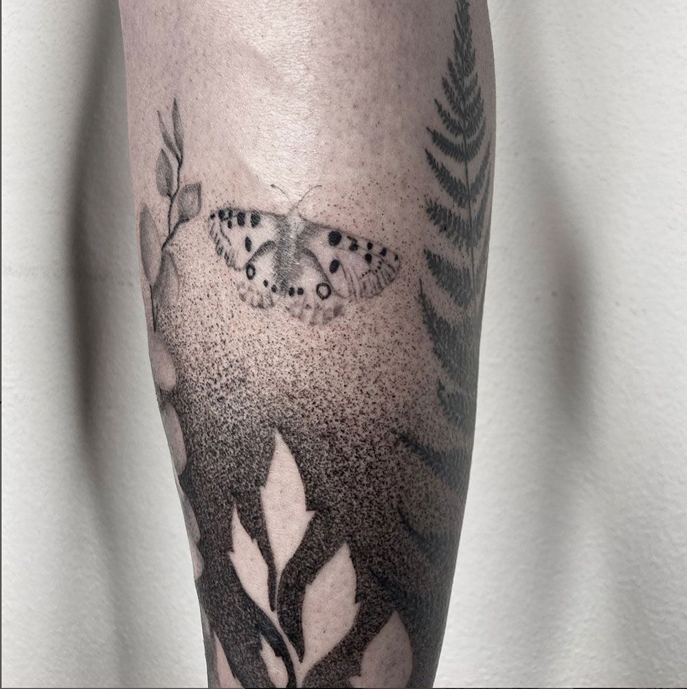 Ein Tattoo von einem Schmetterling und Blättern auf einem Bein