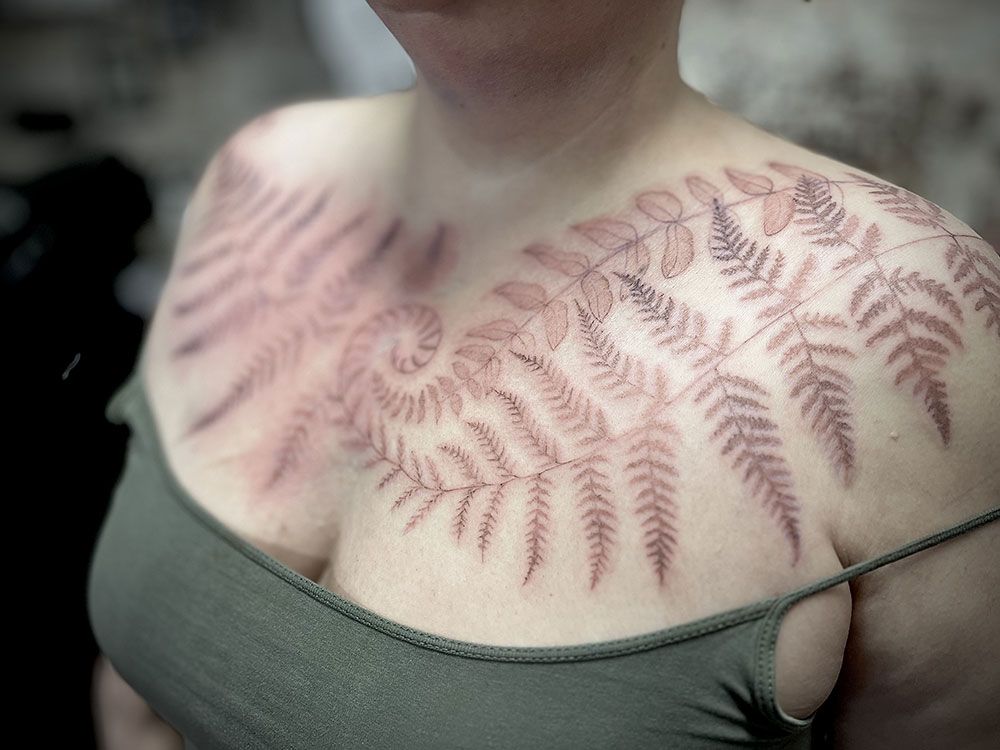 Eine Frau hat ein Farntattoo auf Brust und Schulter.