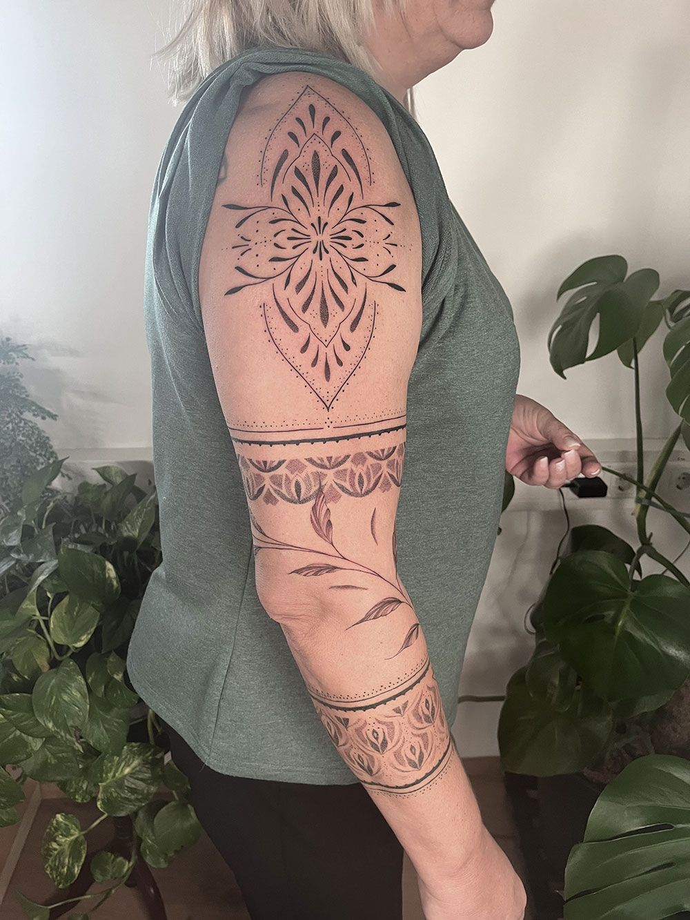 Eine Frau mit einer Tätowierung auf dem Arm steht vor einer Pflanze.