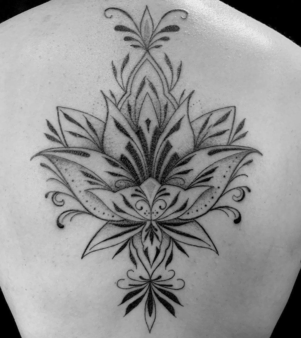 Ein schwarz-weißes Tattoo einer Lotusblume auf dem Rücken einer Person