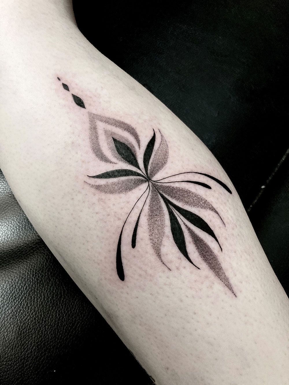 Eine schwarz-weiße Tätowierung einer Blume auf dem Arm einer Person.
