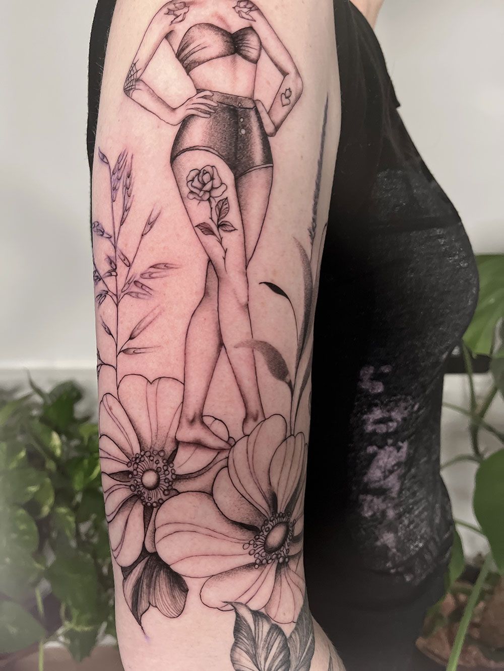 Eine Frau hat eine Tätowierung einer Frau umgeben von Blumen auf ihrem Arm