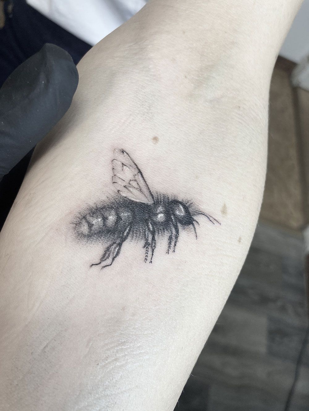 Ein schwarz-weißes Tattoo einer Biene auf dem Arm einer Person