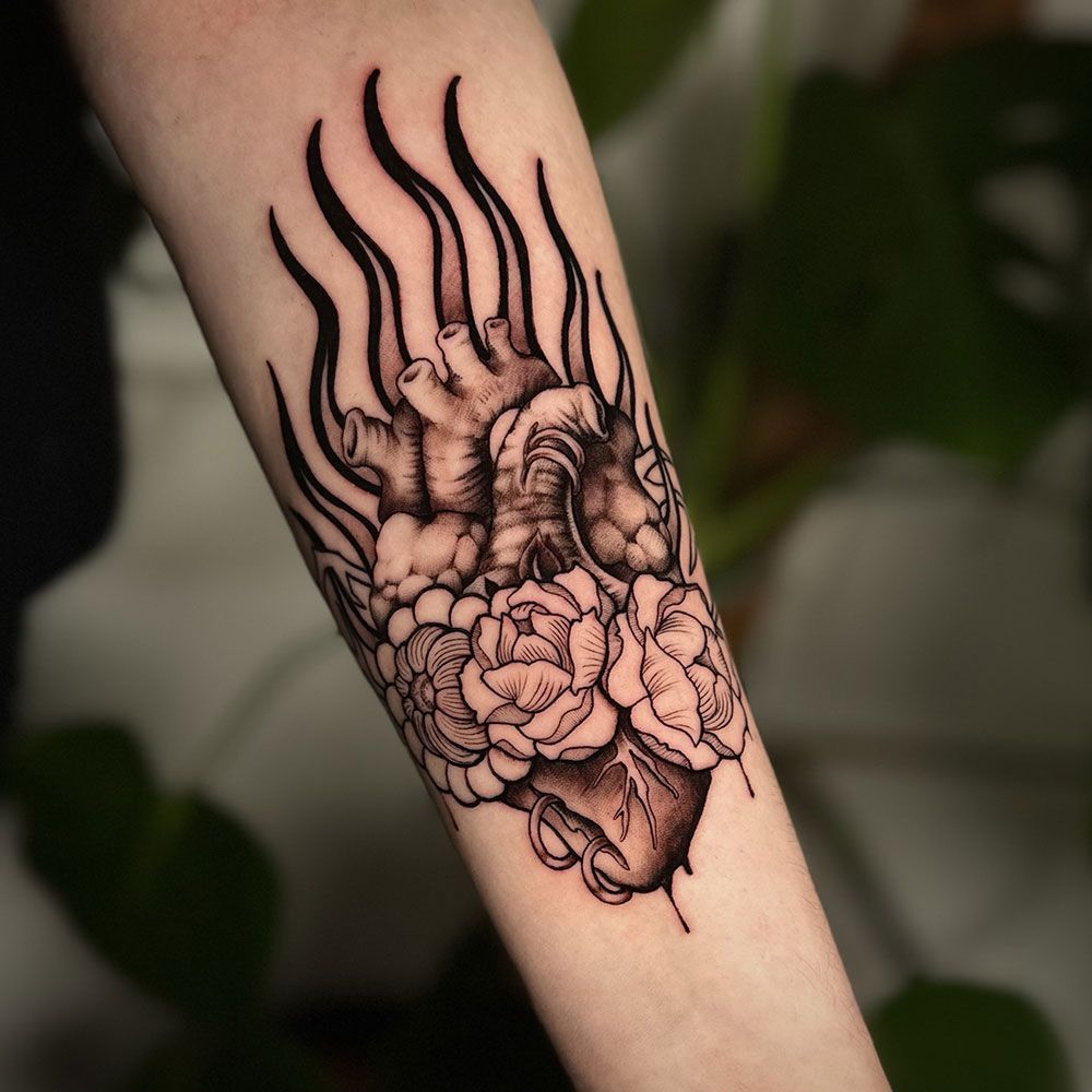 Eine schwarz-weiße Tätowierung eines von Rosen umgebenen Herzens auf dem Unterarm einer Person.