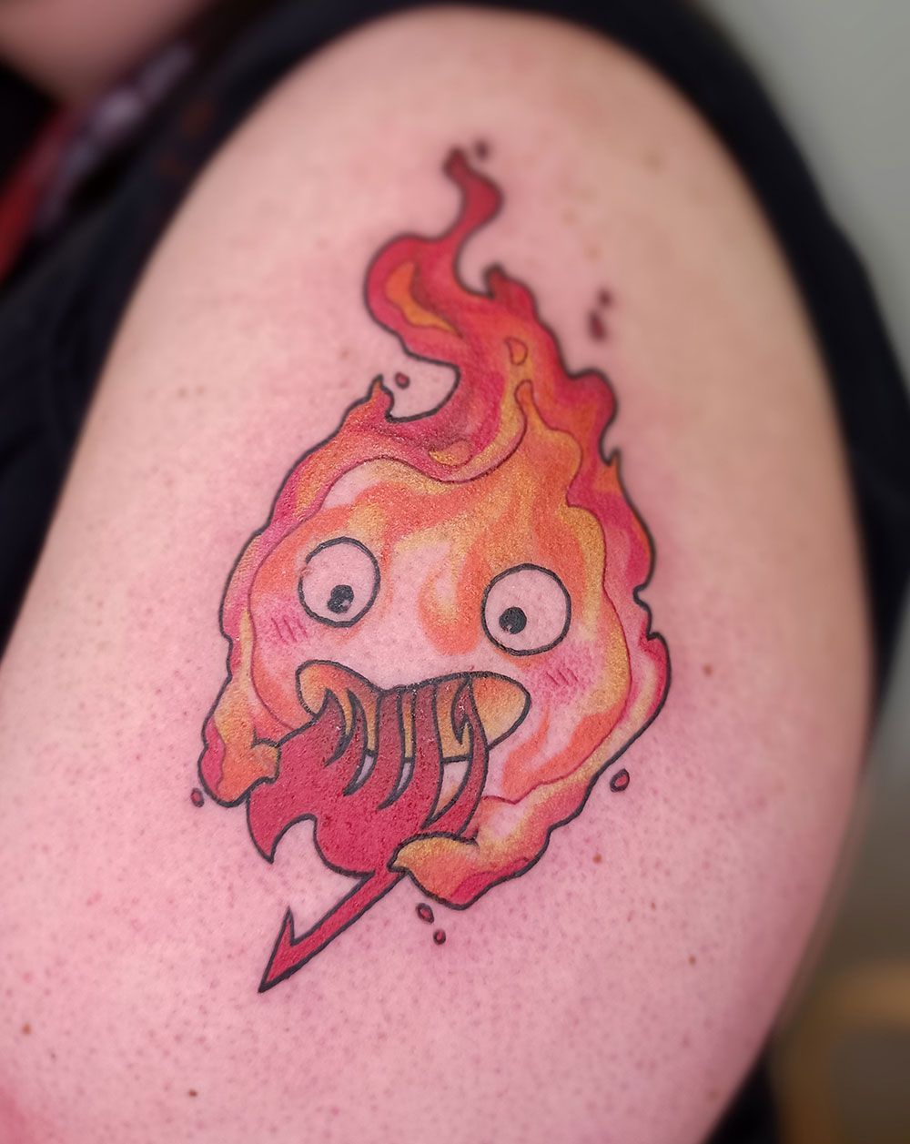 Eine Person hat auf ihrem Arm ein Tattoo von einem Feuerball mit heraushängender Zunge