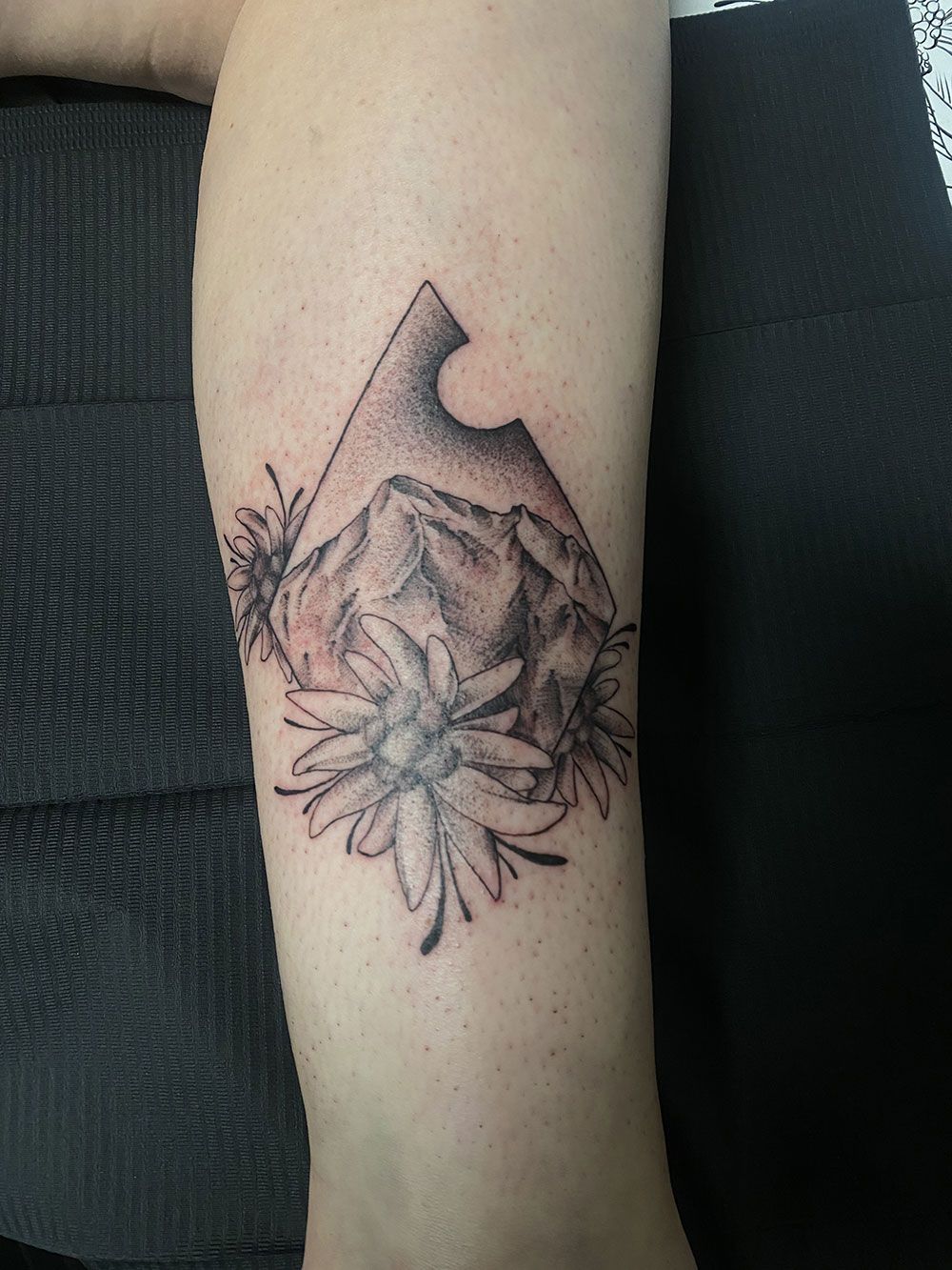 Eine Tätowierung eines Berges und von Blumen auf dem Unterarm einer Person.