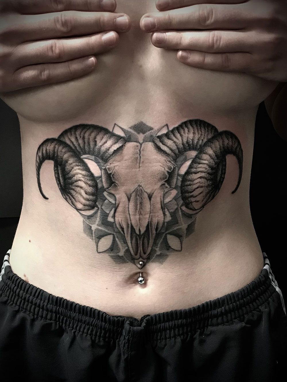 Eine Frau hat ein Tattoo eines Widderschädels auf ihrem Bauch