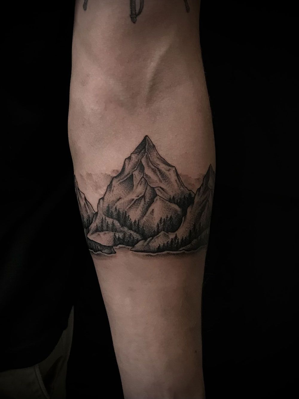 Eine schwarz-weiße Tätowierung eines Berges auf dem Unterarm einer Person.