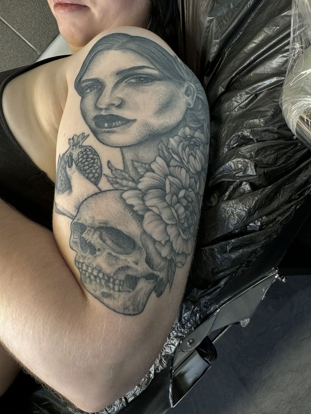 Eine Frau hat eine Tätowierung mit einem Frauengesicht und einem Totenkopf auf ihrem Arm.