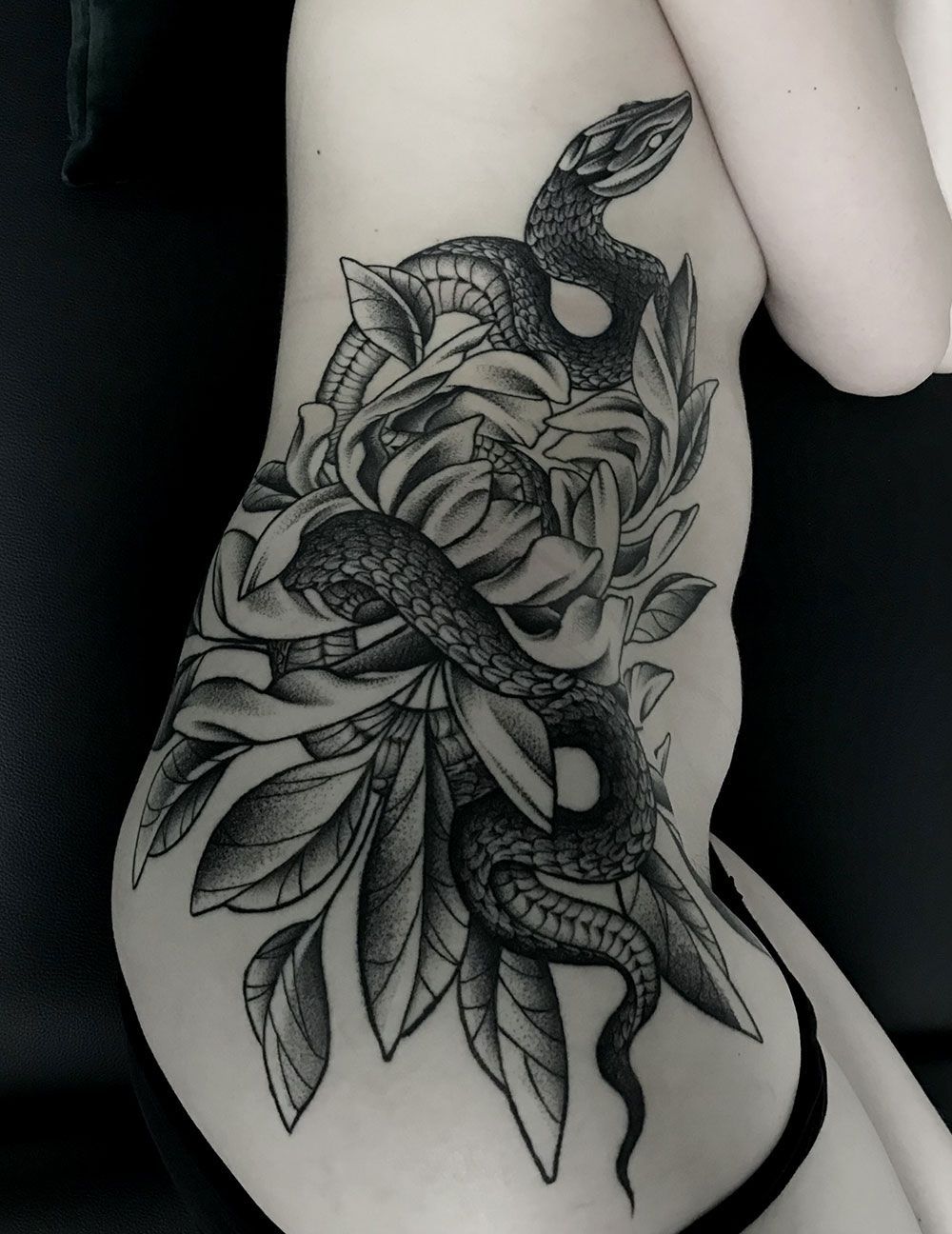 Eine Frau hat an ihrer Seite eine Tätowierung mit einer Schlange und Blumen.