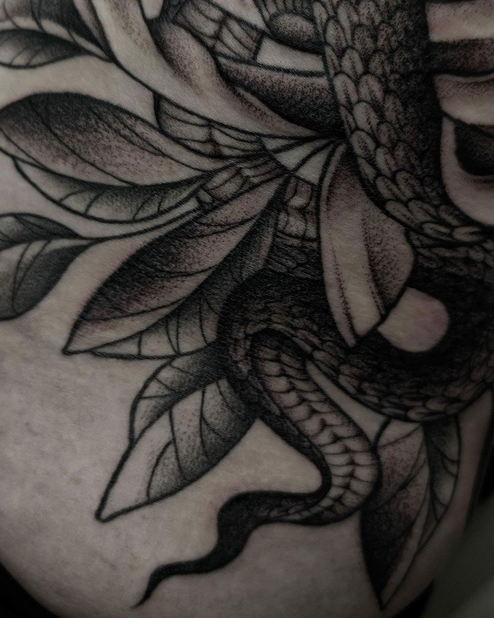 Eine schwarz-weiße Tätowierung einer Schlange und Blättern auf dem Arm einer Person.